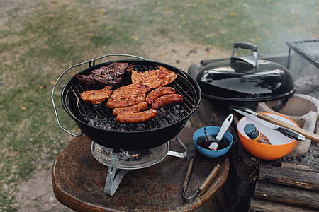 meats and sausages grilled on round black charcoal grill on top of table thumbnail