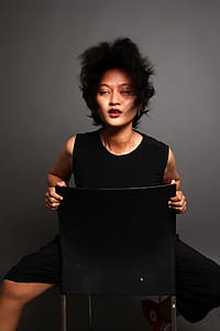 Woman Sitting Backward on Black Chair With Gray Background thumbnail