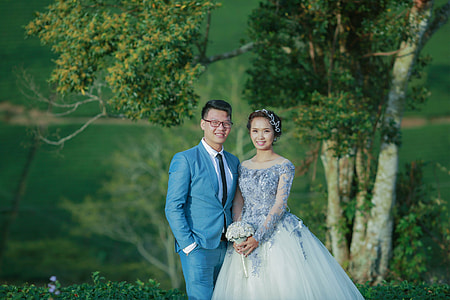 smiling groom and bride standing in front of trees thumbnail