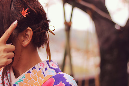 shallow depth of field photo of woman in purple, pink, and orange floral shirt with red maple leaf hair clip thumbnail