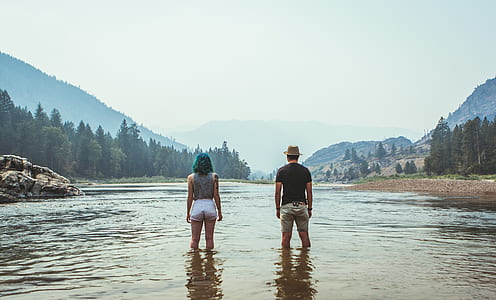 man and woman standing on body of water near trees thumbnail