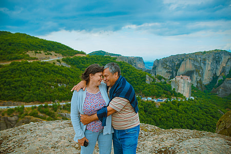 couple standing on mountain top overlooking grass-covered mountains thumbnail