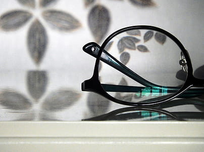 Abstract view of a pair of black rimmed glasses against a floral pattern background with a turquoise light reflection in the lense thumbnail