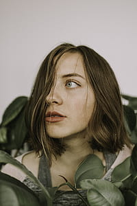 woman in brown scoop-neck shirt surrounded by green plant leaves thumbnail
