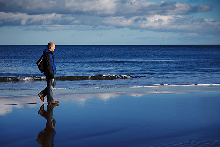 person in blue jacket walking beside seashore at daytime thumbnail