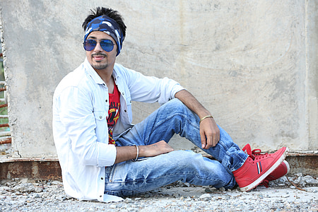 man wearing sunglasses, white sport shirt, blue denim jeans, and red high-top sneakers posing while laying on ground thumbnail