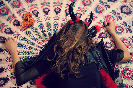 person wearing black dress and devil's horn while lying on area rug thumbnail