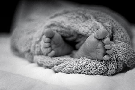 Greyscale Photo Of Human Feet Covered In Knitted Comforter thumbnail