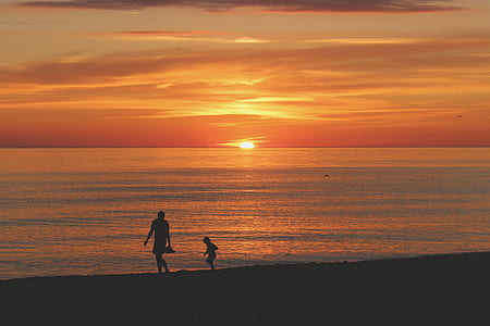 silhouette photo of two person walking on seashore near sea under orange sky during golden hour thumbnail