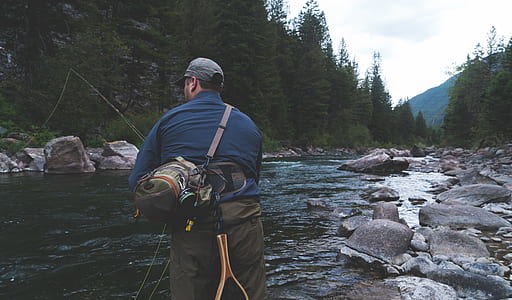 man holding fishing rod near trees thumbnail