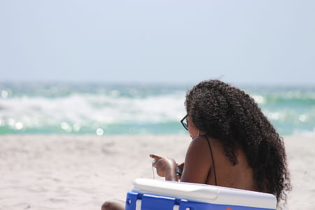 Woman Sitting on Sand Beside Blue and White Cooler Box Near Shore thumbnail