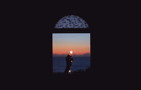 low-light photography of person's hand holding star light near window through clam body of water during golden hour thumbnail