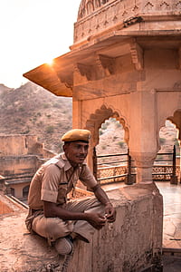 man wearing brown uniform seating on gray concrete wall thumbnail