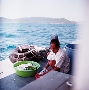 man sitting while cleaning clothes near sea thumbnail