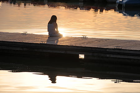 woman in white long-sleeved shirt sits on brown wooden dock thumbnail