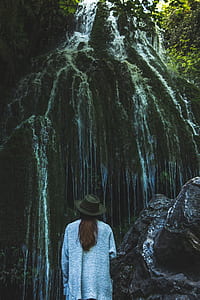 woman in gray cardigan standing near waterfalls during daytime thumbnail