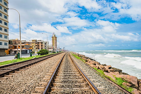 photo of train rails near body of water and buildings thumbnail