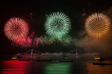 Fireworks under the bridge with boats on body of water thumbnail