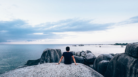 man sitting on rock facing ocean thumbnail