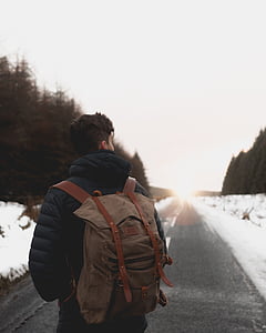 man wearing brown backpack standing on gray road at daytime thumbnail