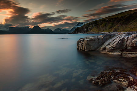 aerial shot of body of water near mountain under cloudy weather thumbnail