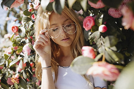 selective focus photography of woman wearing white shirt beside pink rose flower thumbnail