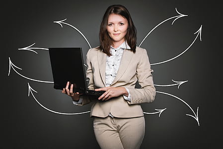 woman wearing grey blazer and grey bottoms smiling while holding laptop computer thumbnail