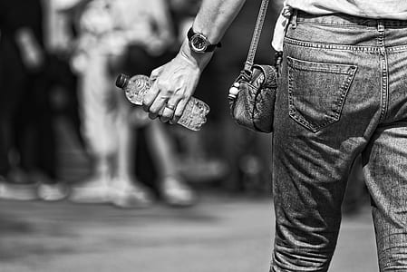person in denim jeans holding bottled of water in greyscale photography thumbnail