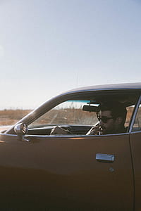 man sitting inside orange car under blue sky thumbnail