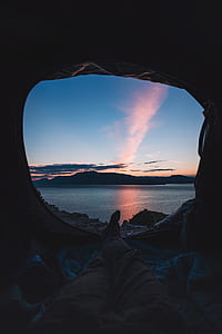 person lying inside tent with overlooking body of water thumbnail