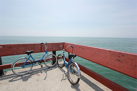 two cruiser bikes parked beside wooden fence overlooking body of water thumbnail