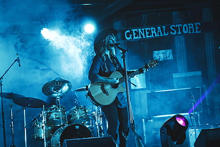 woman singing on stage holding brown wooden guitar thumbnail