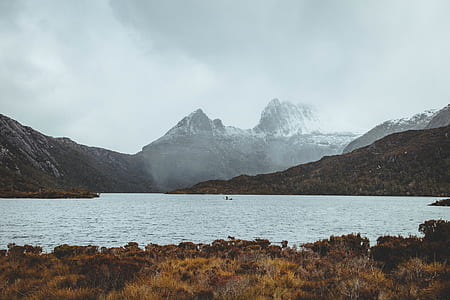 body of water surrounded by mountains under gray sky thumbnail
