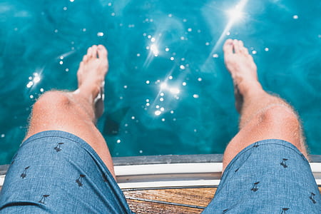 person in blue shorts sitting on dock with body of water thumbnail