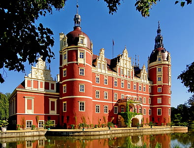 red concrete castle beside body of water under blue sky thumbnail