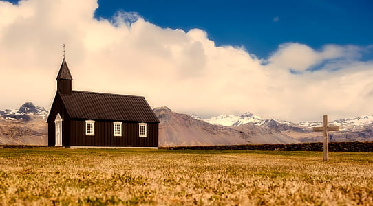 black chapel near mountain under blue and white cloudy sky at daytime thumbnail