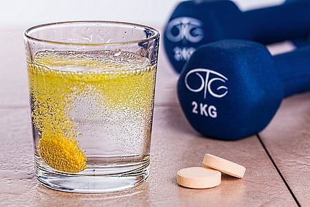 clear rock glass beside two white medication tablets near pair of 2 kg blue fixed dumbbells thumbnail