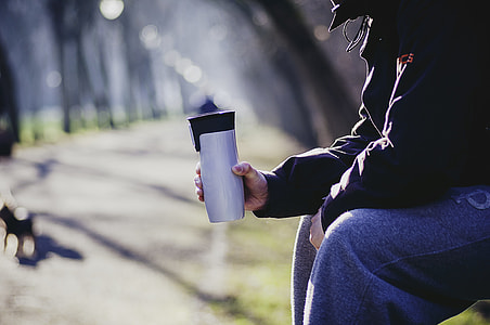 selective focus photography of man sitting on bench holding tumbler thumbnail