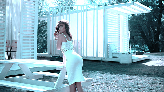 woman wearing white sleeveless dress  arching back in front of white wooden picnic table thumbnail