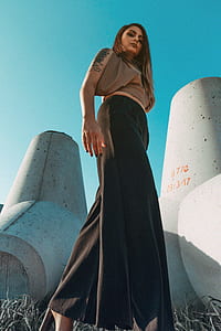 brown haired woman in brown top and black maxi skirt standing near concrete wall thumbnail