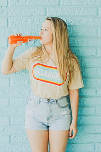 woman drinking on clear glass bottle on front of teal concrete wall thumbnail