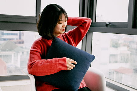black haired woman in red sweater holding blue throw pillow sitting on white armchair thumbnail