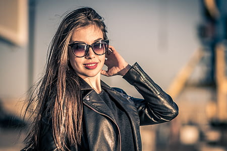selective focus photo of smiling woman holding hair wearing black leather zip-up riding jacket and black cateye sunglasses thumbnail