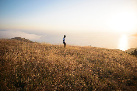 person standing on grass field on hill during daytime thumbnail