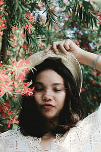 woman with brown hat standing near red petaled flowers thumbnail