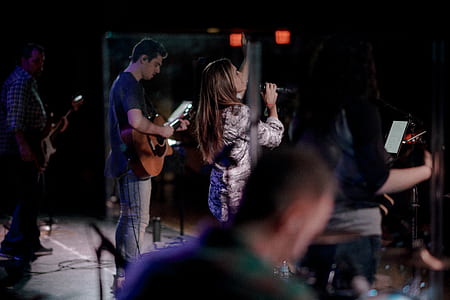 woman singing while lifting her hands surrounded by musicians thumbnail