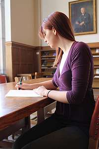 woman wearing purple v-neck shirt siting beside table while writing thumbnail