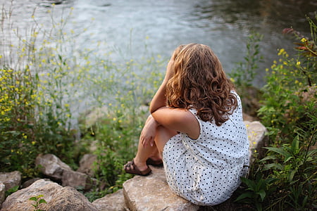 woman sitting on rock facing body of water thumbnail