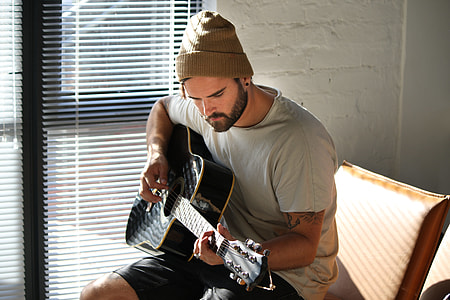 man playing guitar while sitting on brown wooden chair thumbnail