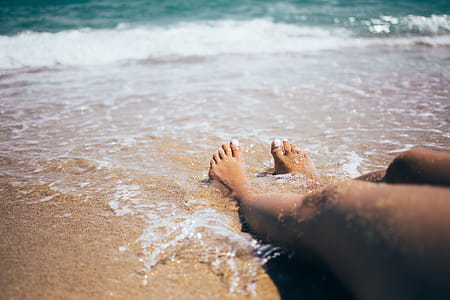 Sandy feet on the beach with waves in the background thumbnail